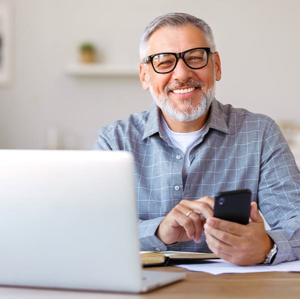 Un homme avec des lunettes et une barbe sourit en utilisant son téléphone.